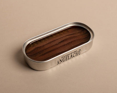 An open tin of anchovies with brown anchovy fillets in olive oil inside and conservas Angelachu written on the side of the silver tin