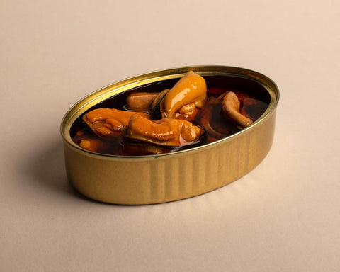 An open gold tin of large orange mussels against a light background