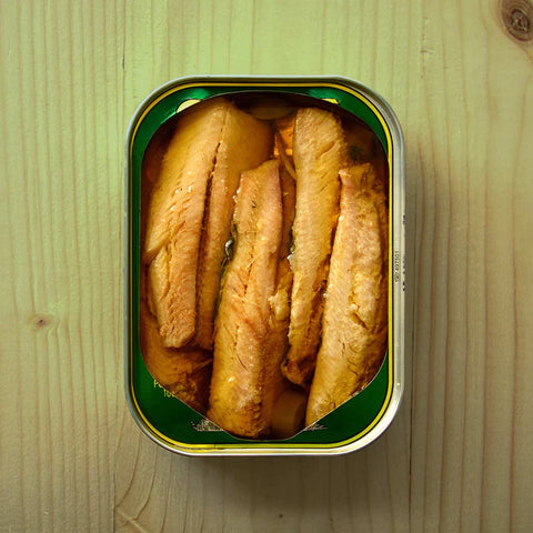 An open tin of sardine fillets in extra virgin olive oil against a light wooden table.