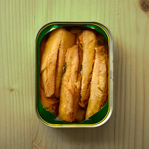 An open tin of sardine fillets in extra virgin olive oil against a light wooden table