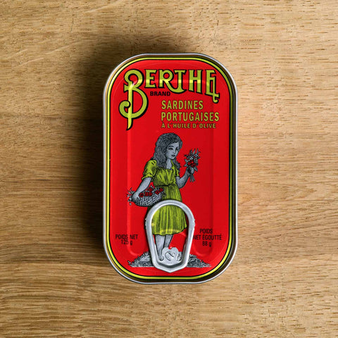 A red tin with Berthe written in yellow above an illustration of a little girl holding a bunch of flowers and wearing a yellow dress.
