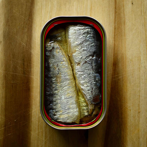 An open tin of sardines in olive oil against a wood background