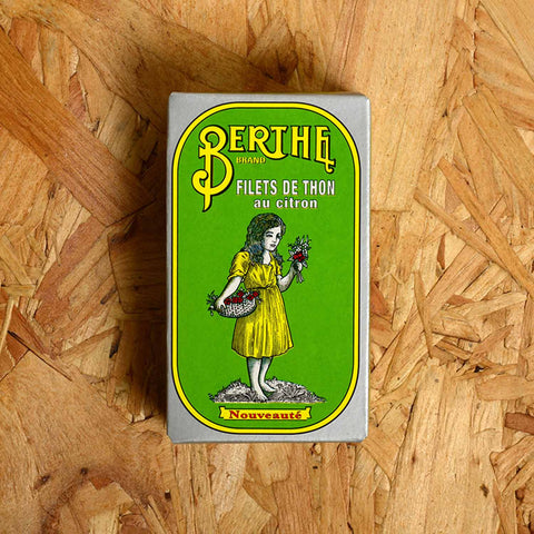 A rectangular box with a green background, silver border, and Berthe written in yellow above an image of a girl in a yellow dress