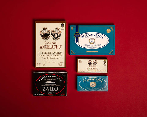 Five tins of Cantabrian anchovies against a red background