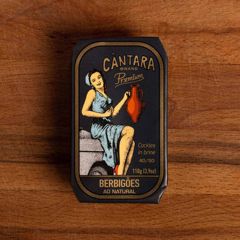 A tin of cockles in black packaging with a gold border and an image of a woman in a blue dress holding an amphora of olive oil