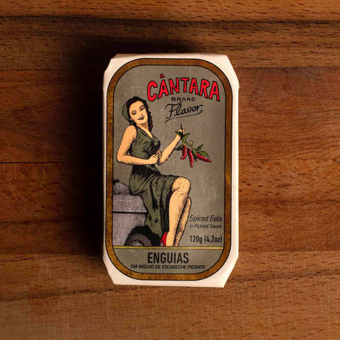 A tin of spicy eels with a woman in a grey dress holding a bunch of red chilli peppers and Cântara written in red lettering on the front