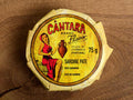 A round tin of sardine pâté in a glossy paper wrap with an illustration of a woman in a red dress beneath Cântara written in red lettering