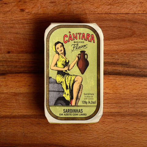 A tin of sardines in a paper wrap with an image of a woman in a yellow dress holding an amphora of olive oil beneath the Cântara logo. 