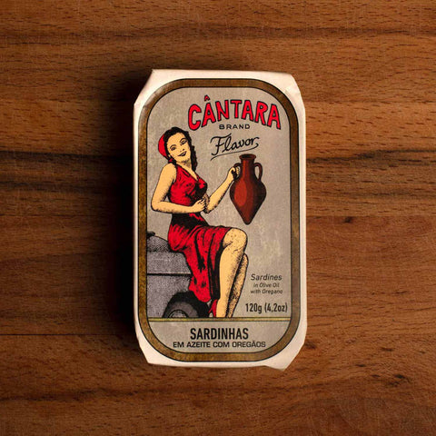A tin of sardines with a paper wrap depicting a woman in a red dress holding an amphora of olive oil. The tin is against a wood background