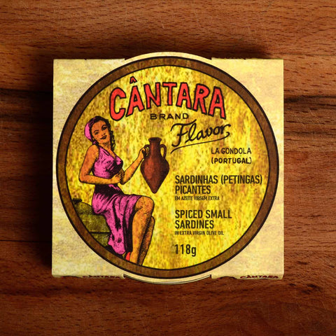 A round tin of small sardines in a card wrap. Cântara is written in red above an image of a woman in a pink dress holding an amphora of olive oil on the packaging