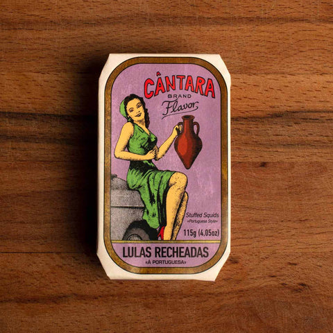 A tin of stuffed squid in a purple paper wrap with a white and gold border. There is an image of a woman in a green dress holding an amphora of olive oil beneath the Cântara logo in red lettering