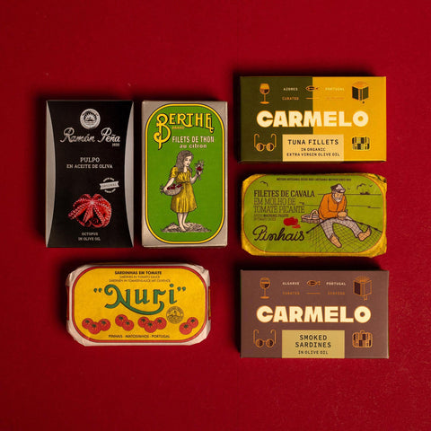 Six vintage Spanish tinned fish boxes arranged on a solid red background. The boxes feature retro designs with illustrations .