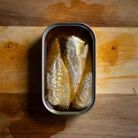 Beautiful tinned Sardines. Perfectly positioned on a pinewood table. Waiting to be enjoyed.