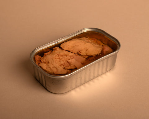 An open tin of cod liver. The tin is silver. On a beige-coloured background.