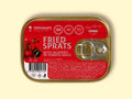 A golden-coloured rectangular tin with a silver ring-pull on the right. The tin is on a pale yellow background. The tin has a red sticker covering its surface with "Fried sprats with jalapeño in tomato sauce" written in white lettering by an image of some tomatoes on the vine and two jalapeño peppers. The ingredients and nutrients are written at the bottom of the label in small white type.