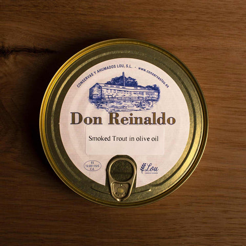 A round gold-coloured tin with a sticker on the front. Don Reinaldo is written on the sticker in gold lettering below a drawing of the cannery. 
