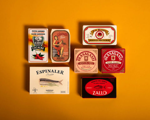 Several tins of fish in brightly-coloured packaging against a yellow background 