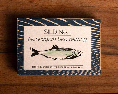 A rectangular box with a blue border and a painting of a herring on the front, against a wood background