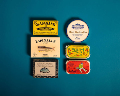 Six brightly coloured tins arranged on a light blue backdrop. 