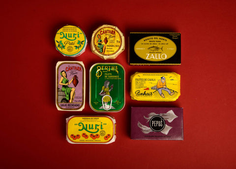 Several brightly-coloured tins of Portuguese and Spanish tinned fish arranged on a red backdrop.