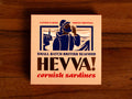 Box containing Cornish sardines from Hevva! The box is illustrated with a fisherman calling out over the Cornish coast with cliffs and a lighthouse in the background. The box is colourful with Hevva! written in golden, embossed lettering  