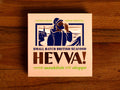 Box containing Cornish monkfish with Aleppo chilli from Hevva! The box is illustrated with a fisherman calling out over the Cornish coast with cliffs and a lighthouse in the background. The box is colourful with Hevva! written in golden, embossed letters  