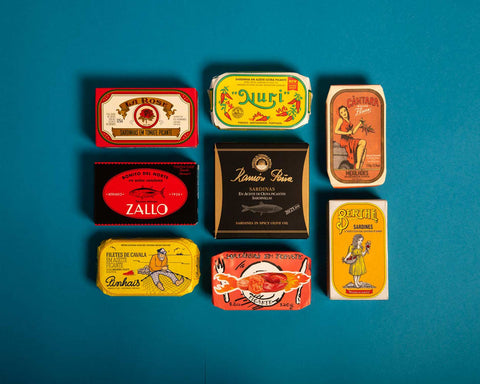 Spanish and Portuguese tinned fish in colourful and classic packaging arranged on a light blue backdrop.