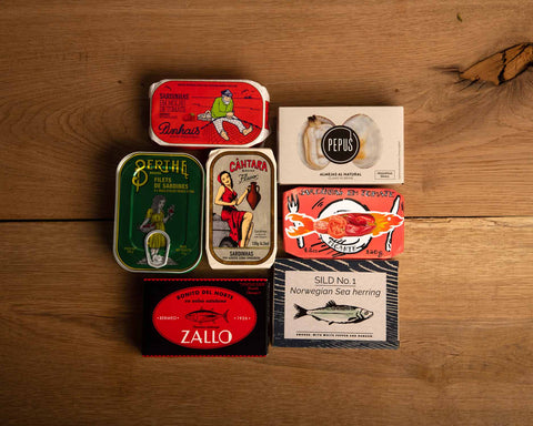 Seven tins with brightly coloured packaging against a wood background.