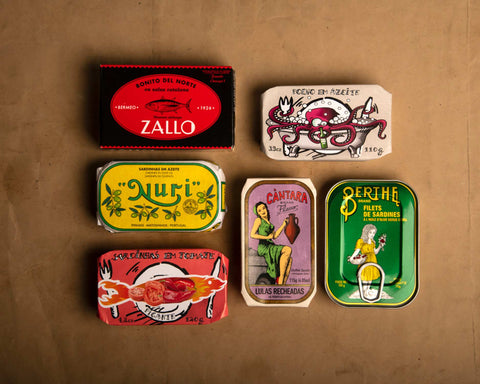 Six brightly-coloured tins arranged on a light brown backdrop.