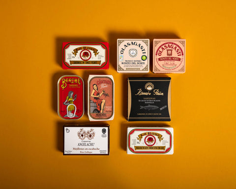 Several tins of Portuguese and Spanish fish in colourful and classic packaging against a yellow background
