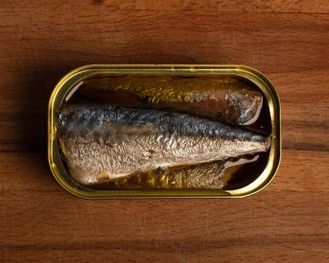 Succulent-looking silvery, skin-on mackerel placed on a dark wooden table.