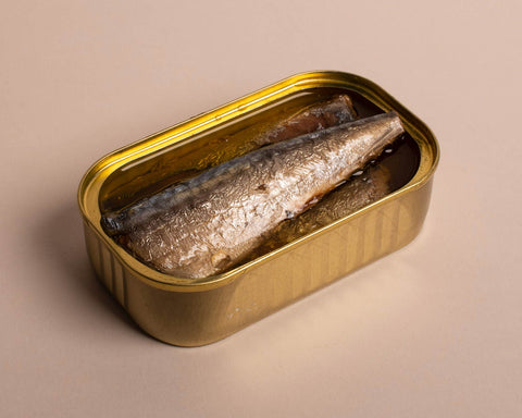 Silvery tinned mackerel in a gold-coloured tin against a pale clear background.
