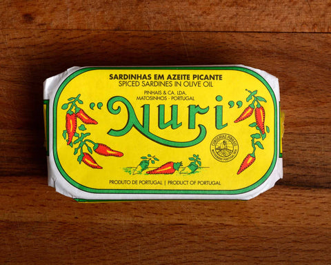 A tin of spicy sardines in a yellow wrap with a white and green border. Nuri is written in green lettering above some red chilli peppers.