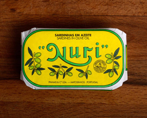 A tin of sardines in a yellow paper wrap with a green and white border. Nuri is written in green lettering above some small olive branches.