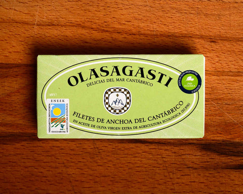 A green rectangular tin of Olasagasti anchovies in extra virgin olive oil against a wood background