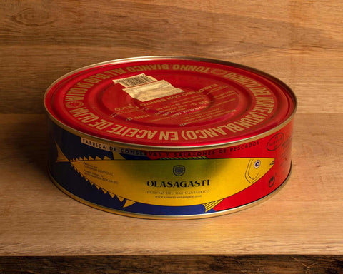 A large circular tin of tuna with a red lid with gold lettering and an image of a golden tuna on the front against a blue and red background.