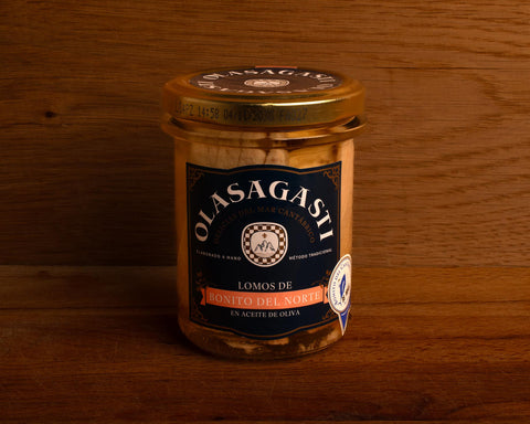 A closed jar of tuna fillets with a gold lid and a blue label with Olasagasti written in white lettering, against a wood background