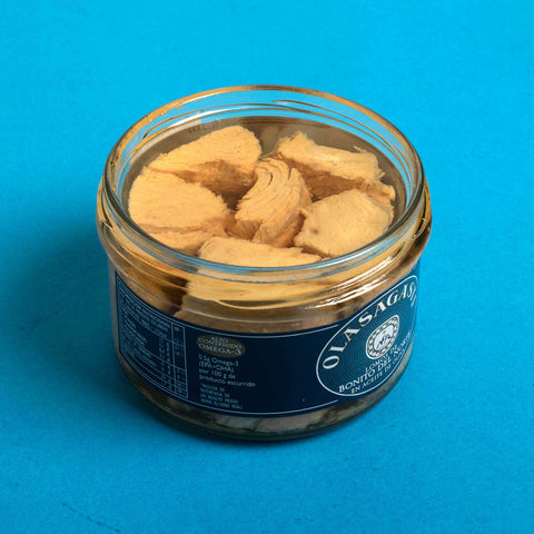 An open jar with tuna fillets in olive oil inside against a light blue background