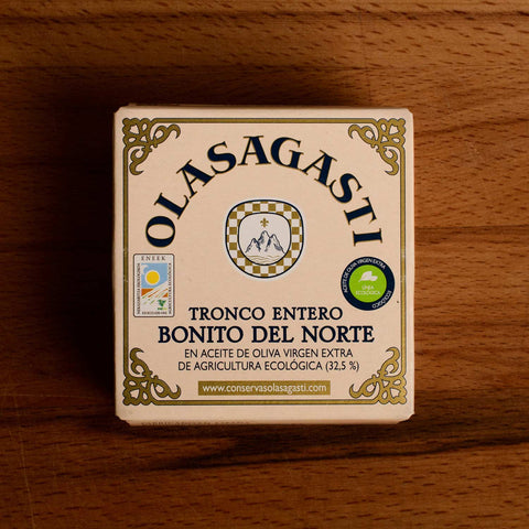 A square tin of tuna with an ornate gold border and Olasagasti written in black lettering against a pale pink background