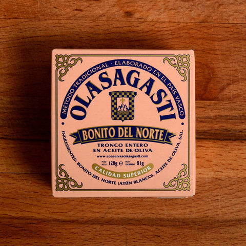 A square tin of tuna with pink packaging and Olasagasti written in blue lettering on the front, against a wood background