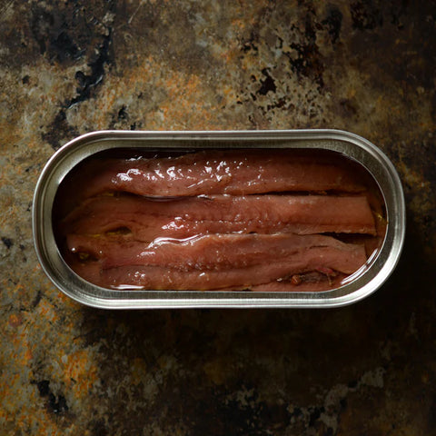 An open tin of anchovies in olive oil, with a powerful granite counter as the backdrop. 