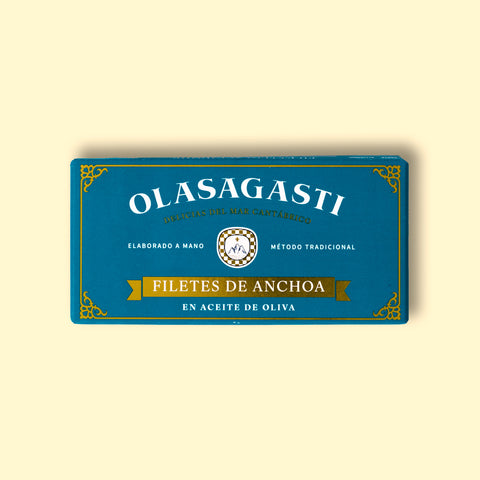 Small Olasagasti anchovy fillets blue packaging on a yellow surface. The design is simple with many details like a Sicilian coat of arms, a golden banner and decorative details on the corners.