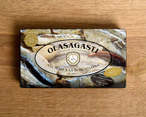 A tin of Olasagasti anchovies with images of anchovies on the front of the packaging, against a wood background