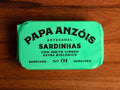 A tin of sardines in organic extra olive oil in light green packaging, featuring the Papa Anzóis brand name on top. 