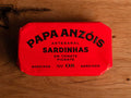 A tin of sardines in spicy tomato sauce in red packaging, with Papa Anzóis displayed at the top. 