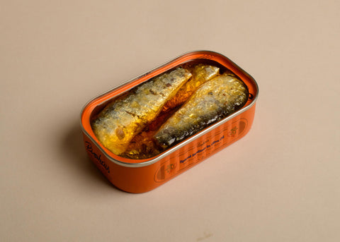 Open tin of sardines in orange-tinted oil in an orange millesime tin from the brand Pinhais.