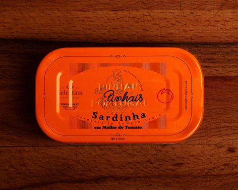 Sardines in tomato sauce inside an orange tin, featuring an illustration of a fisherman, with the Pinhais written below in blue. 