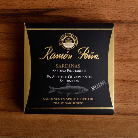 Spicy sardines in black and gold card packaging. Ramón Peña is written in gold lettering above a silver-grey image of a sardine.