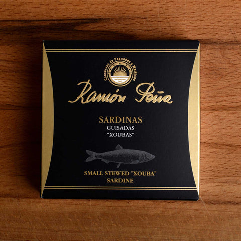 A tin of small sardines in black and gold packaging. Ramón Peña is written in gold lettering above a silver grey image of a sardine