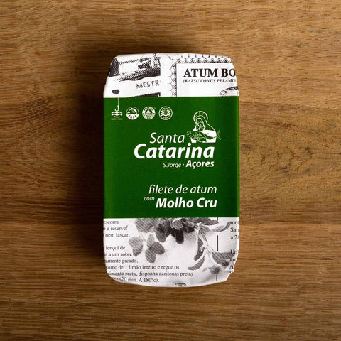 A tin of Santa Catarina tuna in newspaper-style packaging with a green label against a wood background